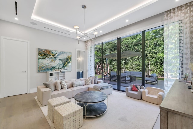 living room featuring a tray ceiling, light hardwood / wood-style flooring, french doors, and an inviting chandelier