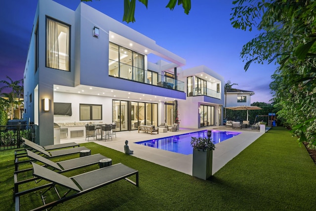 back house at dusk with an outdoor living space, a patio, a balcony, and exterior kitchen