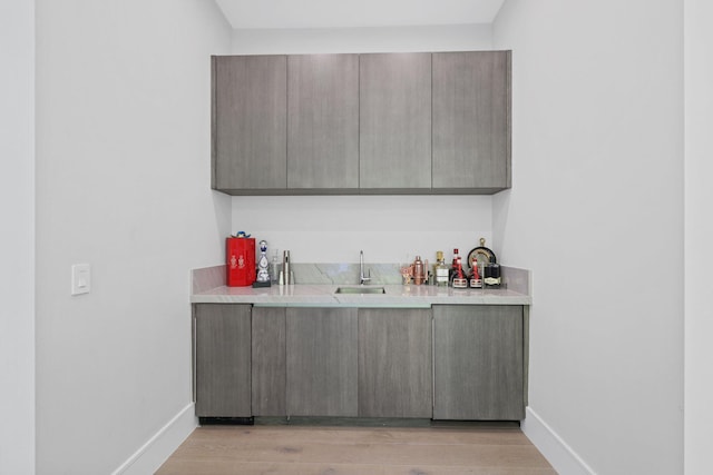 bar featuring gray cabinetry, light hardwood / wood-style floors, and sink