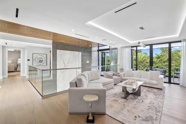 living room with light hardwood / wood-style floors, a raised ceiling, a wall of windows, and french doors