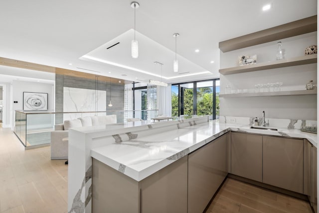 kitchen with light stone countertops, decorative light fixtures, a tray ceiling, and kitchen peninsula