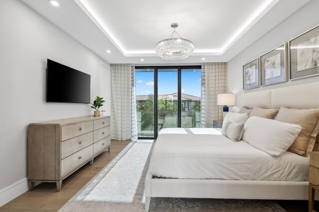 bedroom featuring access to exterior, an inviting chandelier, a raised ceiling, and light hardwood / wood-style floors