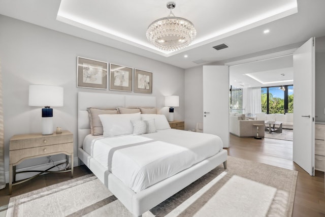 bedroom featuring hardwood / wood-style flooring, a notable chandelier, and a tray ceiling