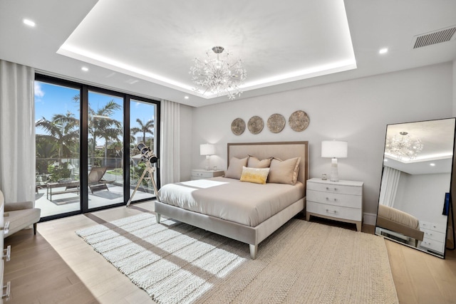 bedroom featuring a raised ceiling, light wood-type flooring, access to outside, and a chandelier