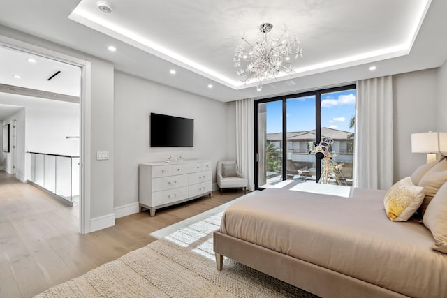 bedroom with a chandelier, access to outside, light hardwood / wood-style floors, and a tray ceiling