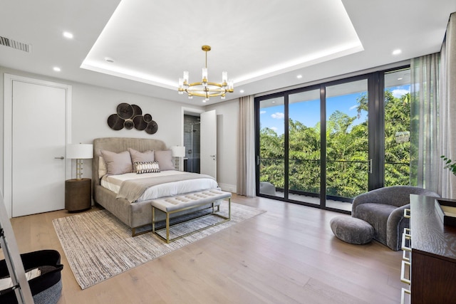 bedroom featuring floor to ceiling windows, a chandelier, light hardwood / wood-style floors, a tray ceiling, and access to outside