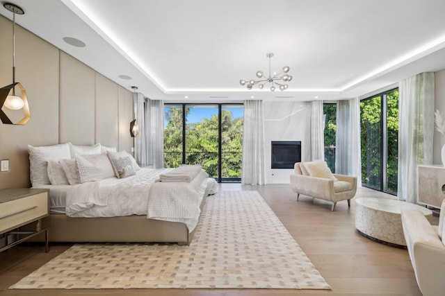 bedroom with a raised ceiling, hardwood / wood-style flooring, a fireplace, a notable chandelier, and a wall of windows