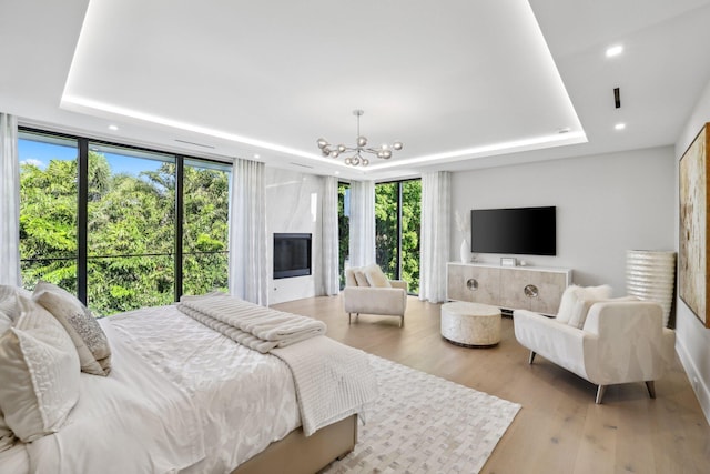 bedroom featuring a notable chandelier, floor to ceiling windows, light hardwood / wood-style flooring, and a tray ceiling