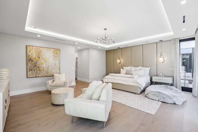 bedroom featuring a tray ceiling, an inviting chandelier, and light wood-type flooring