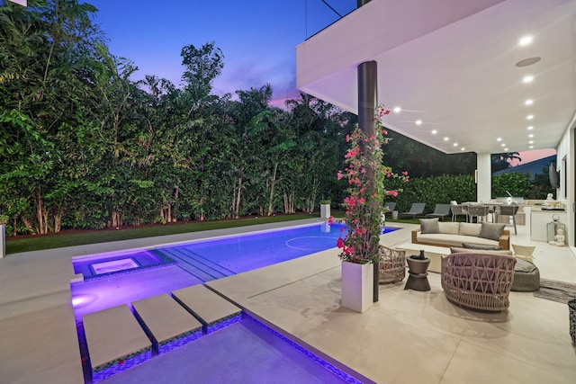 pool at dusk featuring a patio area, an in ground hot tub, exterior kitchen, and an outdoor hangout area