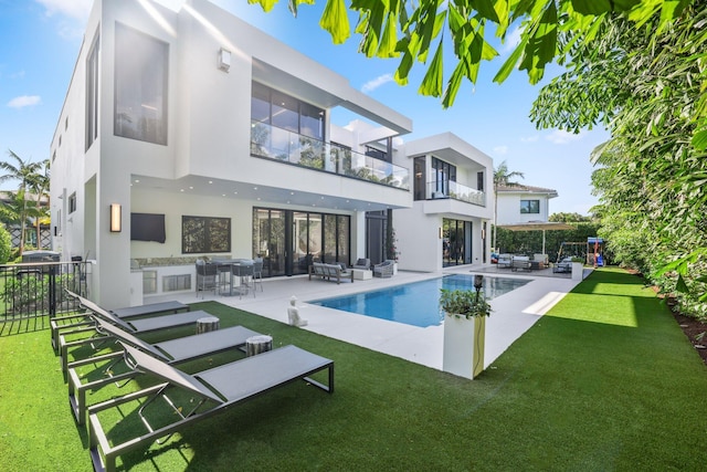 rear view of house with a balcony, outdoor lounge area, a patio, a fenced in pool, and a lawn