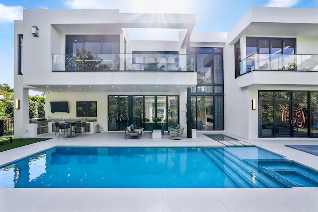 back of house featuring a balcony, exterior kitchen, and a pool with hot tub