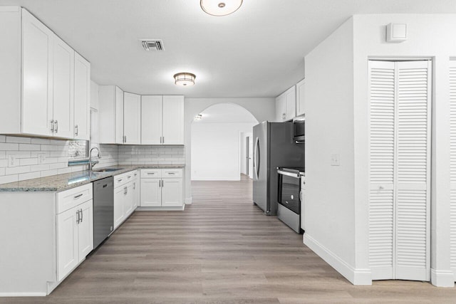 kitchen featuring backsplash, light hardwood / wood-style flooring, light stone counters, white cabinetry, and stainless steel appliances