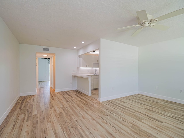 unfurnished living room featuring sink, a textured ceiling, ceiling fan, and light wood-type flooring