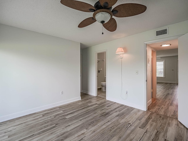 unfurnished bedroom featuring hardwood / wood-style flooring, ensuite bathroom, ceiling fan, and a textured ceiling