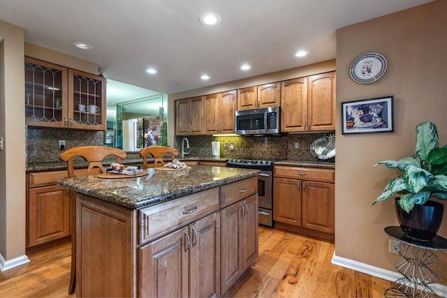 kitchen with light wood-type flooring, a kitchen island, stainless steel appliances, and dark stone counters