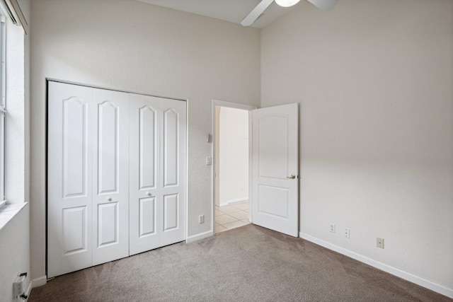 unfurnished bedroom featuring ceiling fan, a towering ceiling, light carpet, and a closet