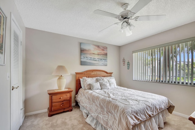 bedroom with ceiling fan, light colored carpet, and a textured ceiling