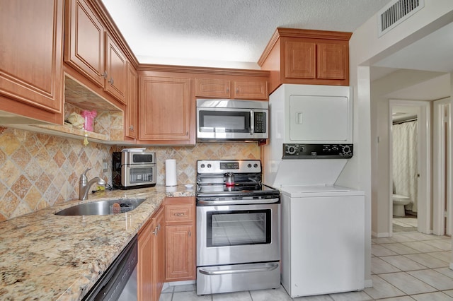 kitchen with light stone countertops, stainless steel appliances, sink, light tile patterned floors, and stacked washer / dryer