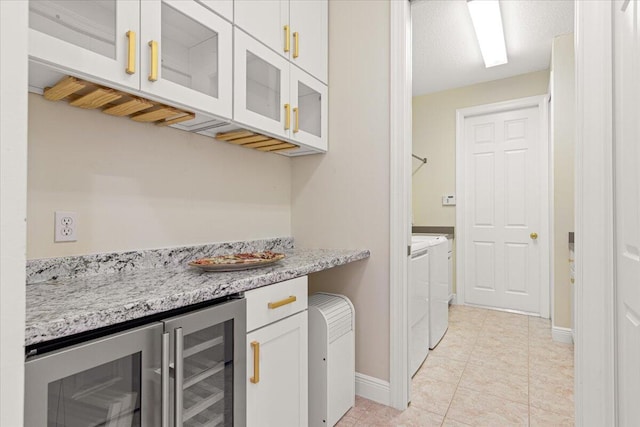 kitchen with white cabinetry, light stone counters, washing machine and clothes dryer, light tile patterned flooring, and beverage cooler