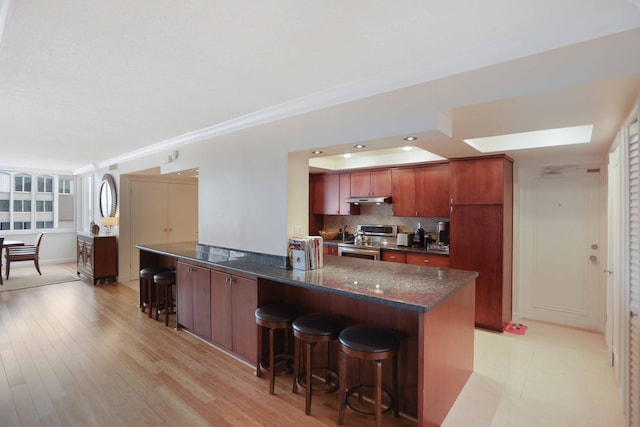 kitchen featuring stainless steel range with electric cooktop, dark stone counters, tasteful backsplash, light hardwood / wood-style floors, and a breakfast bar area