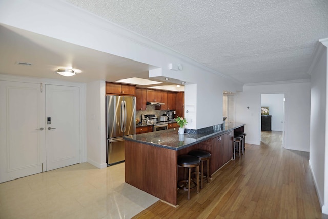 kitchen featuring ornamental molding, a breakfast bar, stainless steel appliances, and light wood-type flooring