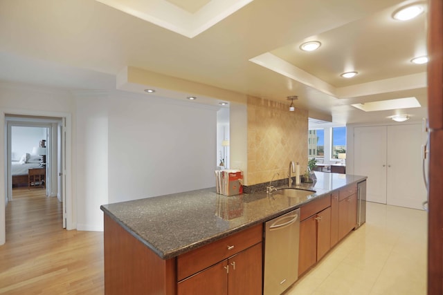 kitchen featuring light wood-type flooring, sink, dark stone countertops, dishwasher, and a center island