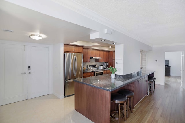 kitchen featuring tasteful backsplash, light hardwood / wood-style flooring, a textured ceiling, a kitchen bar, and appliances with stainless steel finishes