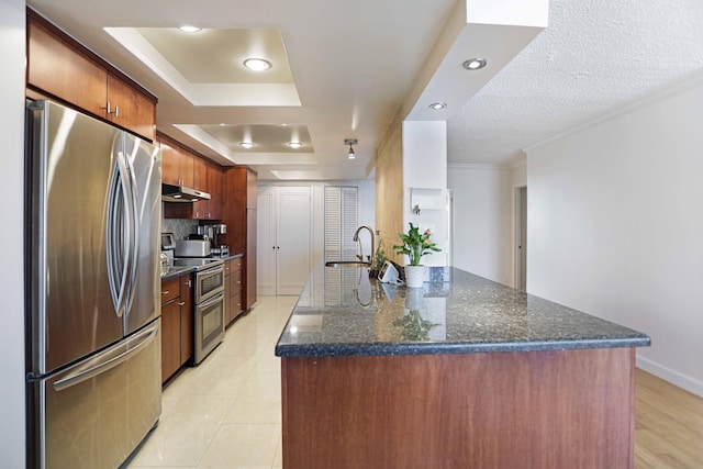 kitchen with a kitchen island with sink, backsplash, light tile patterned floors, appliances with stainless steel finishes, and a tray ceiling