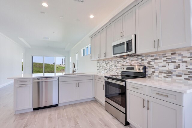 kitchen featuring kitchen peninsula, decorative backsplash, ornamental molding, stainless steel appliances, and sink