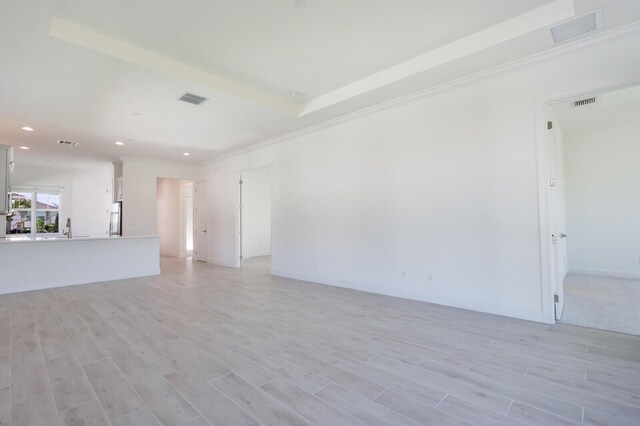 unfurnished living room with light wood-type flooring, a tray ceiling, and sink