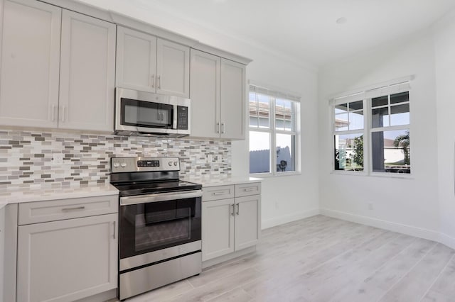 kitchen featuring backsplash, light stone counters, ornamental molding, and stainless steel appliances