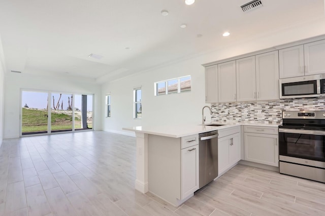 kitchen featuring kitchen peninsula, decorative backsplash, sink, and appliances with stainless steel finishes