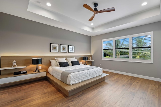 bedroom with a tray ceiling, ceiling fan, and hardwood / wood-style flooring