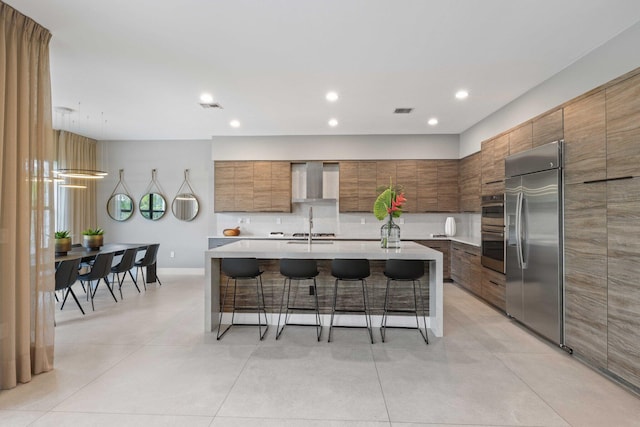 kitchen with a kitchen breakfast bar, tasteful backsplash, stainless steel appliances, wall chimney range hood, and an island with sink