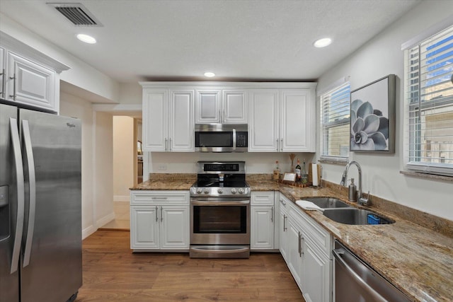 kitchen with sink, appliances with stainless steel finishes, stone counters, hardwood / wood-style flooring, and white cabinets