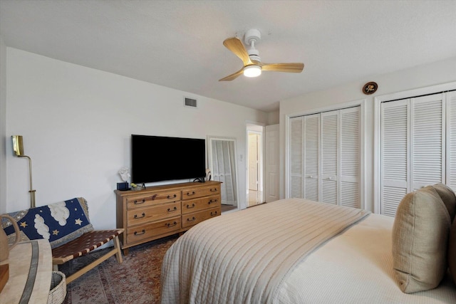 bedroom with multiple closets, ceiling fan, dark carpet, and a textured ceiling