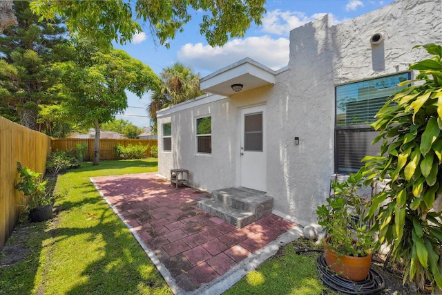 view of exterior entry with a patio and a lawn