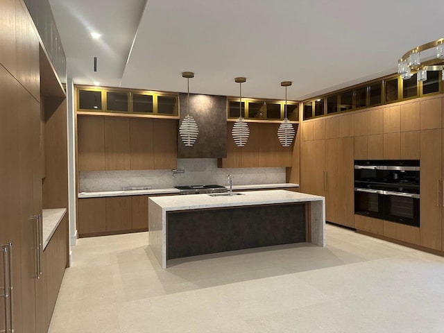 kitchen with multiple ovens, pendant lighting, a center island with sink, and sink