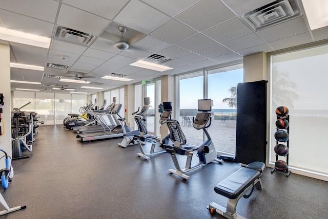 workout area with a water view, a drop ceiling, and a wall of windows