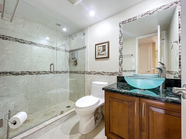 bathroom with tile patterned flooring, toilet, vanity, a shower with shower door, and tile walls