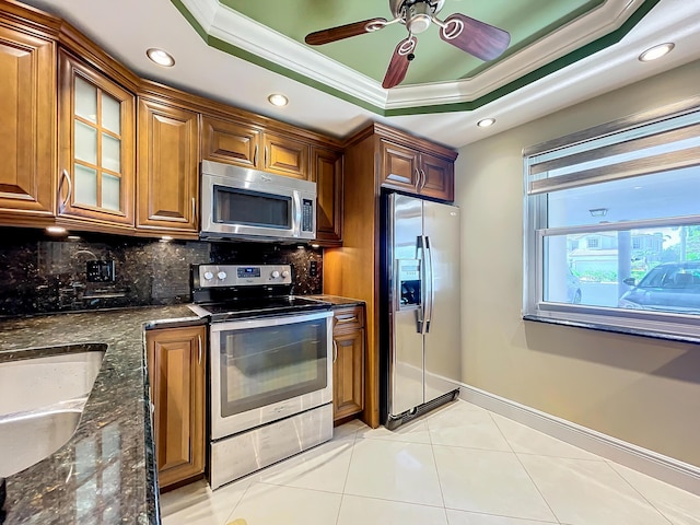 kitchen featuring dark stone counters, ceiling fan, ornamental molding, appliances with stainless steel finishes, and a tray ceiling