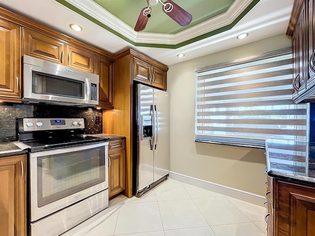 kitchen featuring tasteful backsplash, ornamental molding, stainless steel appliances, a tray ceiling, and dark stone countertops