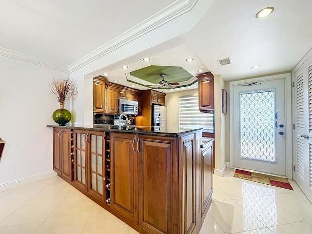 kitchen with kitchen peninsula, appliances with stainless steel finishes, a tray ceiling, light tile patterned flooring, and ornamental molding