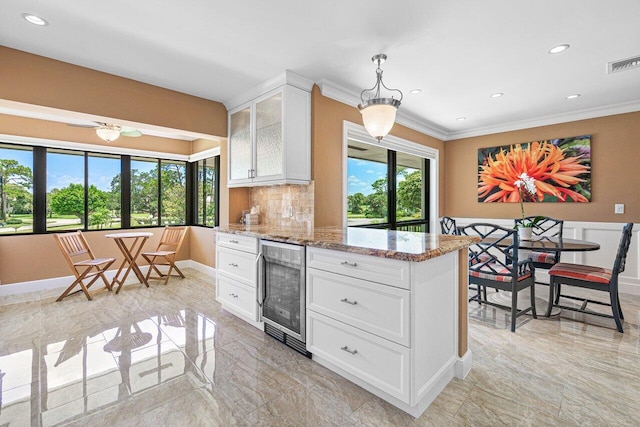 kitchen featuring white cabinets, hanging light fixtures, decorative backsplash, light stone countertops, and beverage cooler