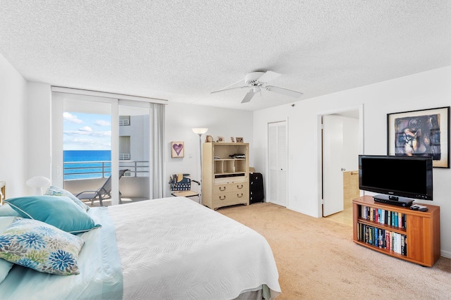 bedroom featuring ceiling fan, access to exterior, a textured ceiling, and a water view