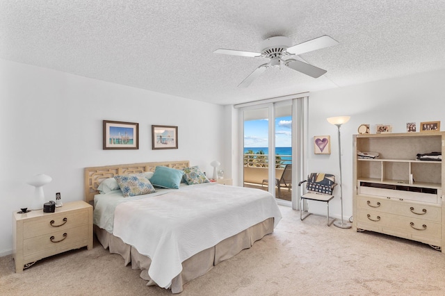 bedroom with ceiling fan, access to exterior, a water view, a textured ceiling, and light carpet