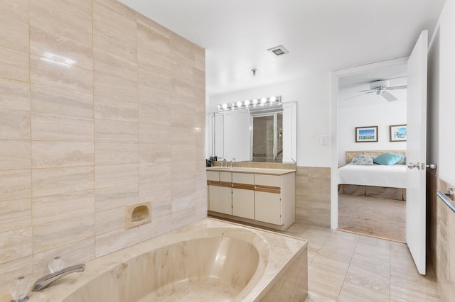 bathroom with tiled bath, vanity, tile walls, ceiling fan, and tile patterned floors