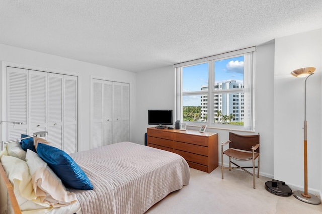 carpeted bedroom featuring a textured ceiling and multiple closets