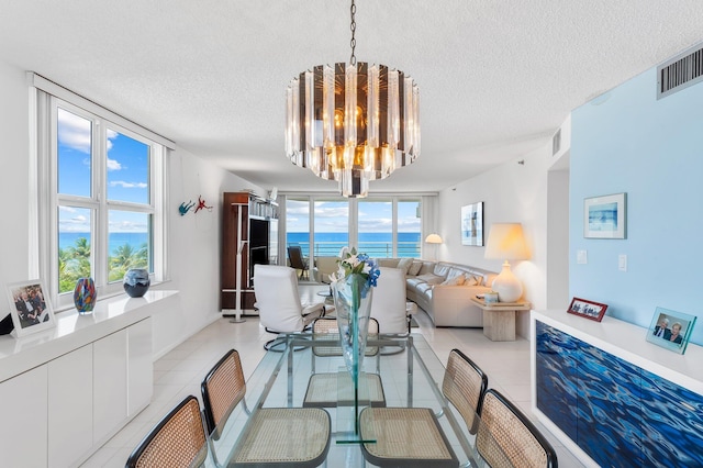 tiled dining space featuring a water view, an inviting chandelier, and a textured ceiling